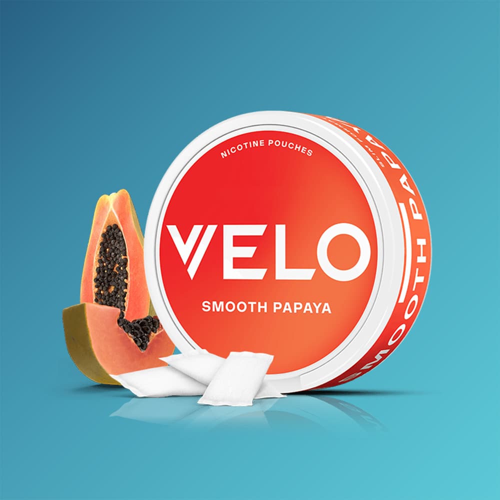 A round container of VELO Smooth Papaya nicotine pouches next to a halved papaya and three loose pouches.